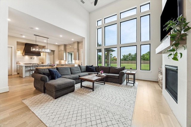 15714 Park Poetry Ct, Cypress, TX 77433 - living room featuring a glass covered fireplace, light wood finished floors, healthy amount of natural light, a high ceiling, and recessed lighting