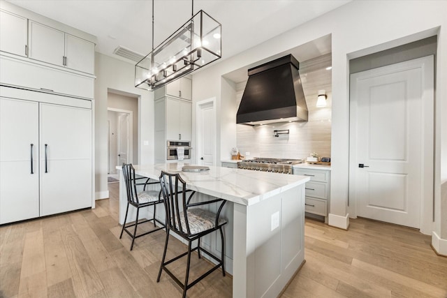 15714 Park Poetry Ct, Cypress, TX 77433 - kitchen featuring wall chimney range hood, light wood finished floors, a breakfast bar area, backsplash, and a chandelier