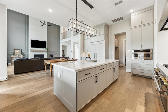 15714 Park Poetry Ct, Cypress, TX 77433 - kitchen featuring light wood-style floors, appliances with stainless steel finishes, a center island with sink, light stone countertops, and pendant lighting