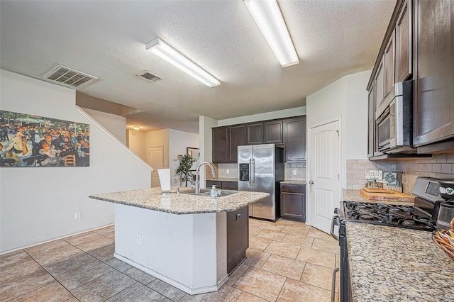 4006 Vicenza Ave, Katy, TX 77493 - kitchen featuring appliances with stainless steel finishes, a textured ceiling, dark brown cabinets, decorative backsplash, and an island with sink