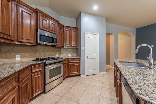 3211 Rock Brook Falls Ln, League City, TX 77573 - kitchen with stainless steel appliances, backsplash, light stone countertops, arched walkways, and light tile patterned floors