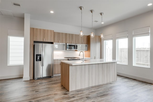 4402 Santorini Ln, Houston, TX 77045 - kitchen with appliances with stainless steel finishes, light countertops, light wood-style flooring, decorative backsplash, and a center island with sink