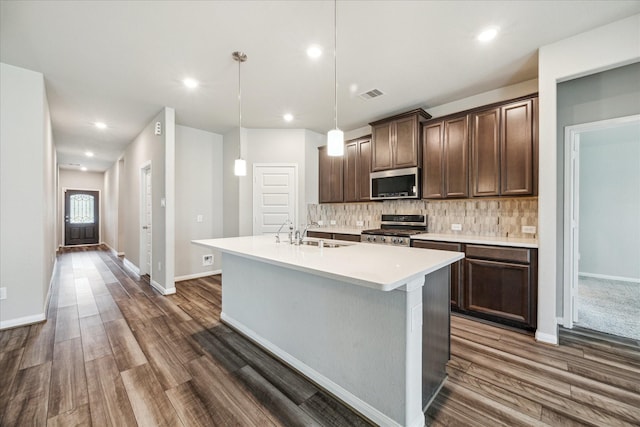 7222 Melrose Ln, Rosharon, TX 77583 - kitchen with appliances with stainless steel finishes, dark wood-style flooring, backsplash, dark brown cabinetry, and a kitchen island with sink