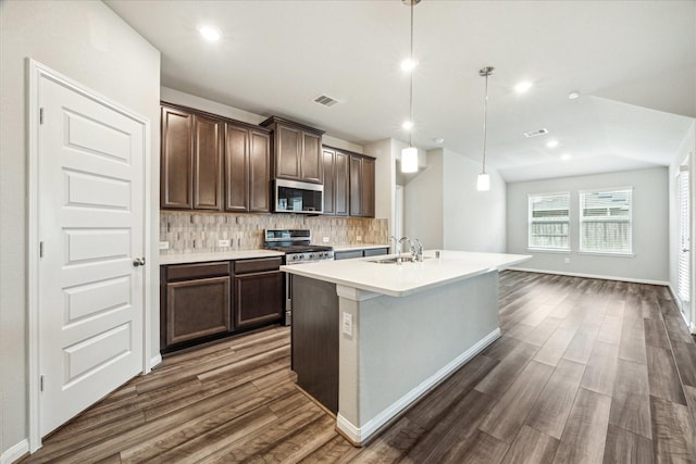 7222 Melrose Ln, Rosharon, TX 77583 - kitchen with stainless steel appliances, tasteful backsplash, dark wood-type flooring, dark brown cabinets, and a center island with sink