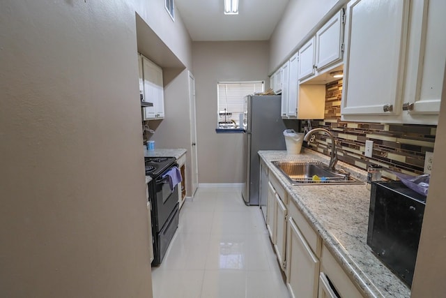 7264 Regency Square Ct, Houston, TX 77036 - kitchen featuring black range with electric cooktop, decorative backsplash, light stone counters, light tile patterned floors, and freestanding refrigerator
