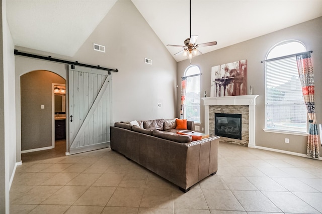 3817 Dunlavy Dr, Pearland, TX 77581 - living room featuring a barn door, ceiling fan, arched walkways, light tile patterned floors, and a stone fireplace