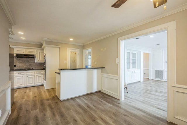 18318 Widcombe Dr, Houston, TX 77084 - kitchen featuring dark countertops, a decorative wall, light wood-type flooring, ornamental molding, and under cabinet range hood