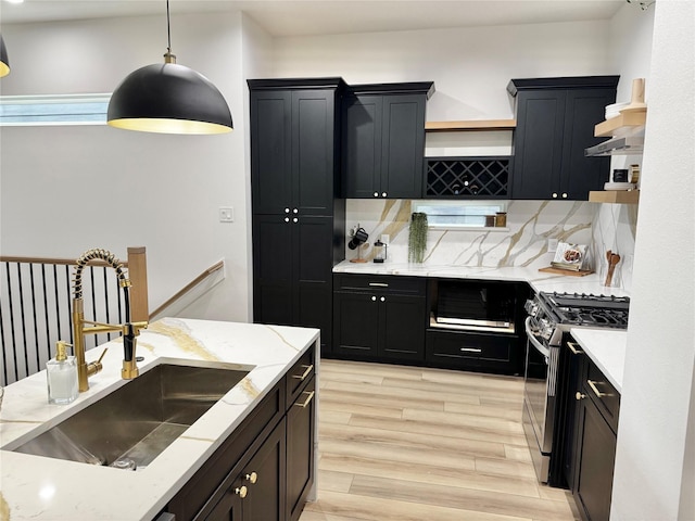 308 E 36th St, Houston, TX 77018 - kitchen featuring gas stove, dark cabinetry, light wood-style flooring, decorative backsplash, and wall chimney exhaust hood