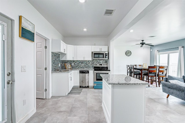 4018 6th St, Galveston, TX 77554 - kitchen featuring appliances with stainless steel finishes, a center island, light stone counters, a ceiling fan, and decorative backsplash