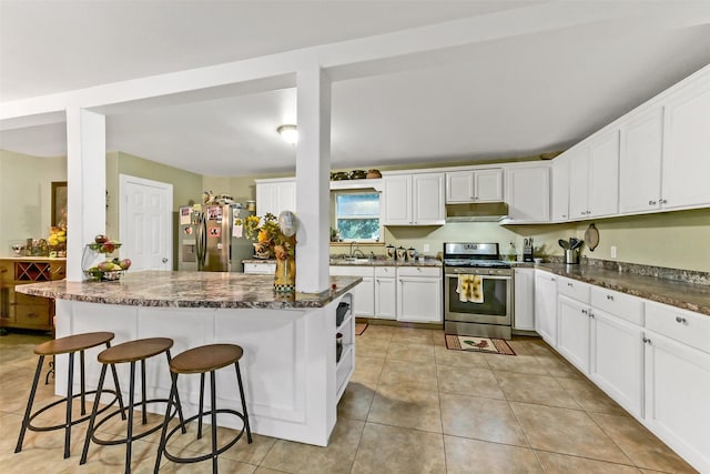 19757 Dorris Dr, Magnolia, TX 77355 - kitchen with stainless steel appliances, under cabinet range hood, white cabinets, a breakfast bar area, and light tile patterned floors