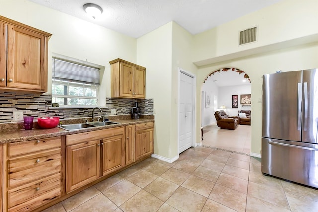 19757 Dorris Dr, Magnolia, TX 77355 - kitchen with freestanding refrigerator, backsplash, arched walkways, light tile patterned floors, and dark countertops