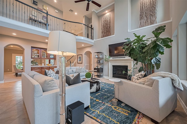 18315 Cape Lookout Way, Humble, TX 77346 - living room with arched walkways, ceiling fan, a high ceiling, a glass covered fireplace, and tile patterned floors