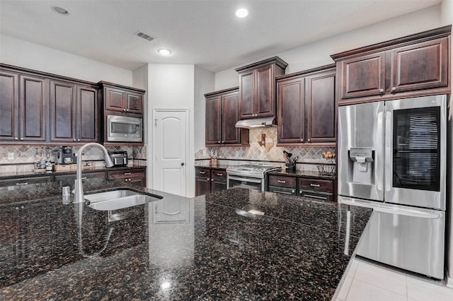 2302 Lakecrest Gardens Dr, Katy, TX 77493 - kitchen with stainless steel appliances, under cabinet range hood, dark brown cabinetry, backsplash, and dark stone countertops