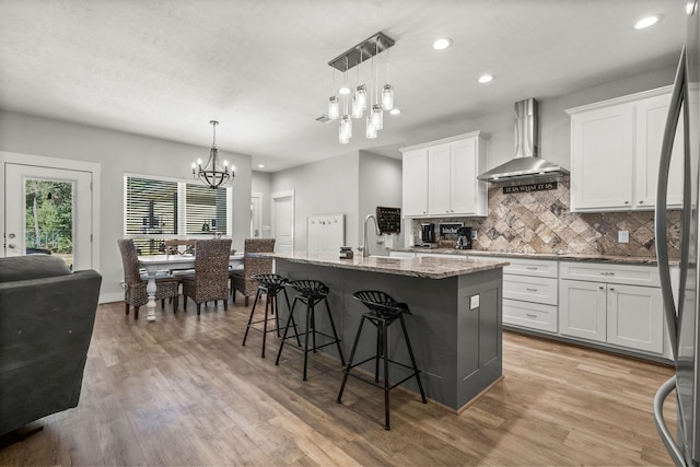 468 Brahman, Onalaska, TX 77360 - kitchen with wall chimney range hood, a chandelier, light wood-type flooring, decorative backsplash, and light stone counters