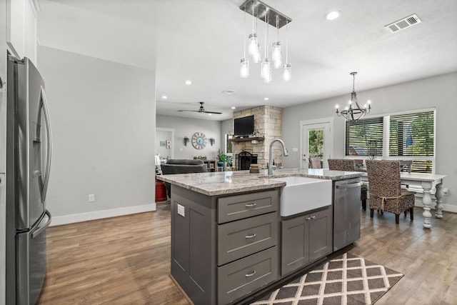 468 Brahman, Onalaska, TX 77360 - kitchen featuring appliances with stainless steel finishes, gray cabinetry, a stone fireplace, light stone countertops, and wood finished floors