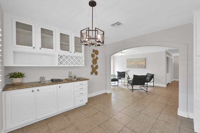 4310 Wigton Dr, Houston, TX 77096 - kitchen featuring arched walkways, dark stone counters, glass insert cabinets, light tile patterned floors, and white cabinets