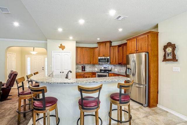 130 Canary Ln, Coldspring, TX 77331 - kitchen with stainless steel appliances, decorative backsplash, brown cabinetry, arched walkways, and a breakfast bar area