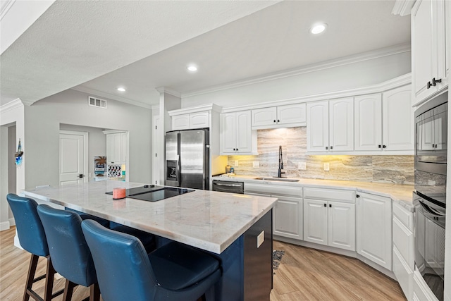 3114 Canterbury Ln, Montgomery, TX 77356 - kitchen featuring stainless steel appliances, ornamental molding, a kitchen island, light wood finished floors, and a kitchen bar