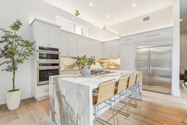 2013 Persa St, Houston, TX 77019 - kitchen with stainless steel appliances, light stone counters, backsplash, light wood-style flooring, and a center island