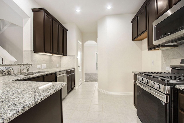 2311 Langley Dr, Rosharon, TX 77583 - kitchen with stainless steel appliances, arched walkways, light stone countertops, dark brown cabinetry, and tasteful backsplash
