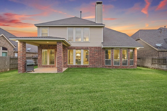 19831 Indigo Key Ct, Cypress, TX 77433 - back of property at dusk featuring a patio, a fenced backyard, brick siding, a chimney, and a shingled roof