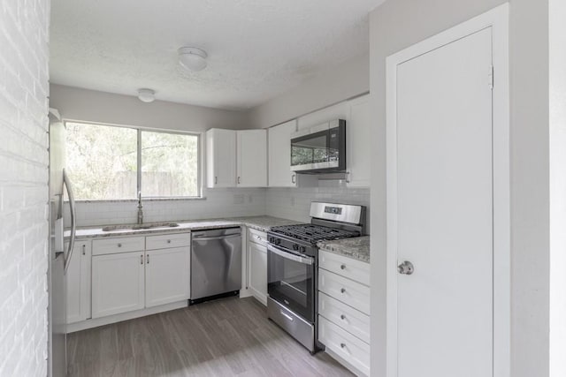 15803 Cerca Blanca Dr, Houston, TX 77083 - kitchen featuring appliances with stainless steel finishes, white cabinets, light wood finished floors, a textured ceiling, and decorative backsplash