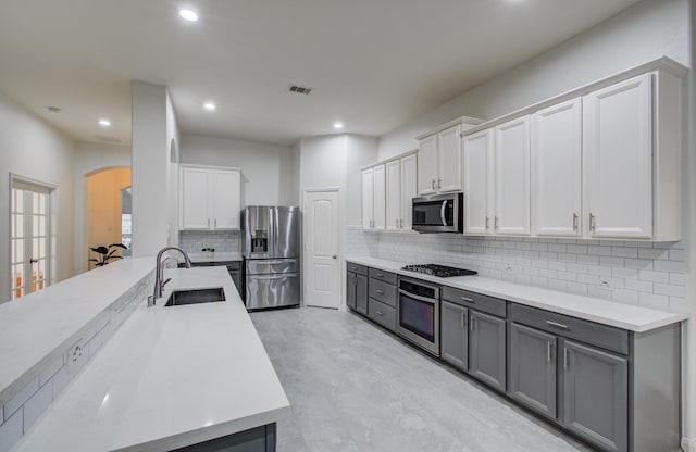 4639 Regal Shadow Ln, Sugar Land, TX 77479 - kitchen with stainless steel appliances, arched walkways, gray cabinetry, decorative backsplash, and recessed lighting