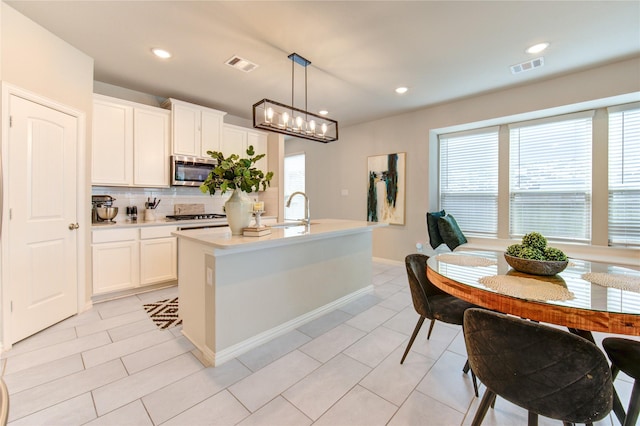 17715 White Lightning Way, Spring, TX 77379 - kitchen with stainless steel microwave, decorative backsplash, gas stovetop, light countertops, and an island with sink