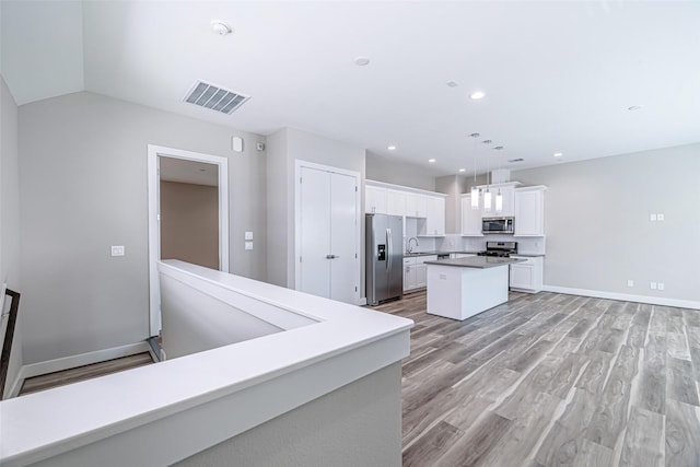 240 Julia St Unit D, Houston, TX 77022 - kitchen with stainless steel appliances, white cabinetry, a center island, light wood-style flooring, and hanging light fixtures