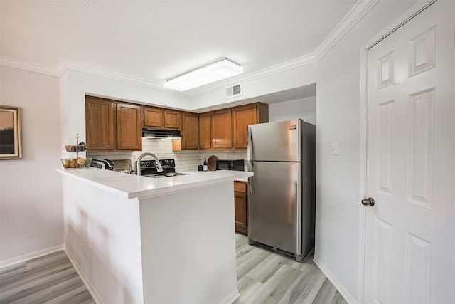 2300 Old Spanish Trl Unit 1060, Houston, TX 77054 - kitchen featuring freestanding refrigerator, under cabinet range hood, light wood-style floors, brown cabinets, and a peninsula