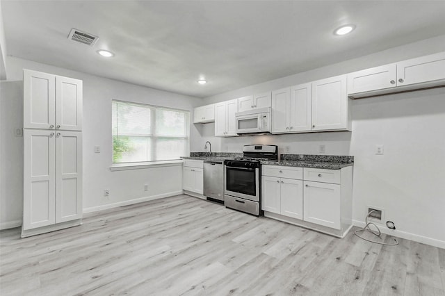 408 Commanche Rd, Conroe, TX 77316 - kitchen with appliances with stainless steel finishes, light wood finished floors, white cabinetry, recessed lighting, and dark stone countertops