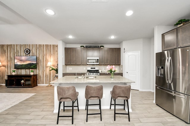 5206 Wyatt James Ln, Brookshire, TX 77423 - kitchen with appliances with stainless steel finishes, dark brown cabinetry, a kitchen bar, light stone countertops, and an island with sink