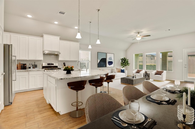 8426 Kari Bend Cir, Richmond, TX 77407 - kitchen featuring stainless steel appliances, ceiling fan, under cabinet range hood, a breakfast bar, and decorative backsplash