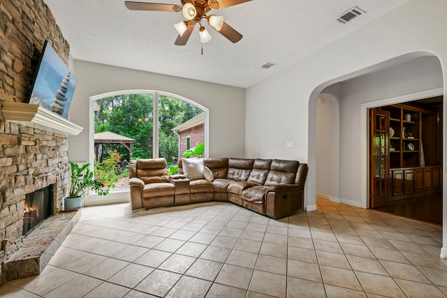 10530 Clubhouse Cir, Magnolia, TX 77354 - living room with light tile patterned floors, a textured ceiling, ceiling fan, arched walkways, and a fireplace