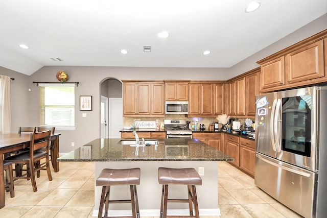 6810 Hunters Trace Ln, Baytown, TX 77521 - kitchen featuring stainless steel appliances, light tile patterned floors, a breakfast bar, arched walkways, and a kitchen island with sink