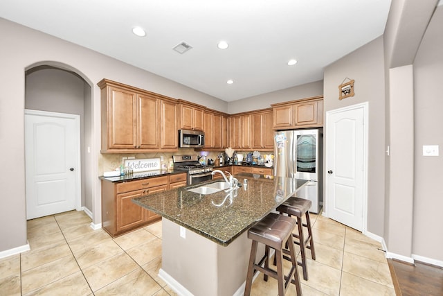 6810 Hunters Trace Ln, Baytown, TX 77521 - kitchen featuring stainless steel appliances, dark stone counters, light tile patterned flooring, a kitchen island with sink, and a kitchen breakfast bar