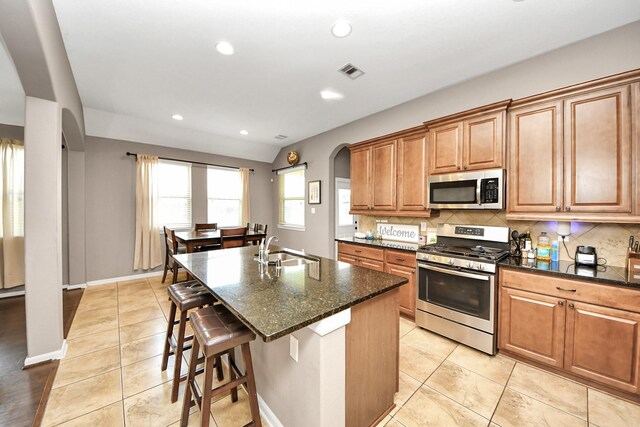 6810 Hunters Trace Ln, Baytown, TX 77521 - kitchen with stainless steel appliances, arched walkways, decorative backsplash, light tile patterned flooring, and brown cabinetry