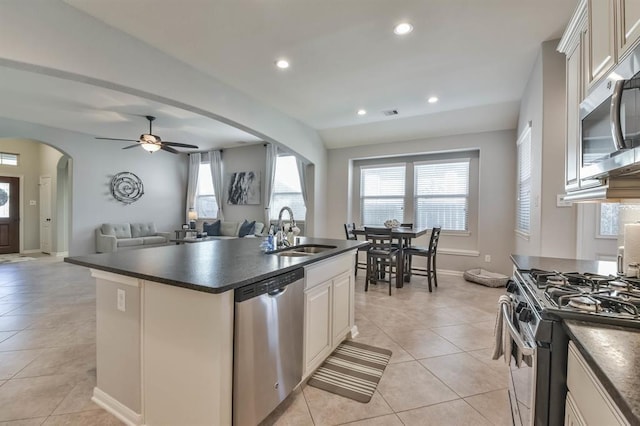 8922 Pinenut Dr, Cypress, TX 77433 - kitchen featuring stainless steel appliances, dark countertops, arched walkways, a center island with sink, and plenty of natural light