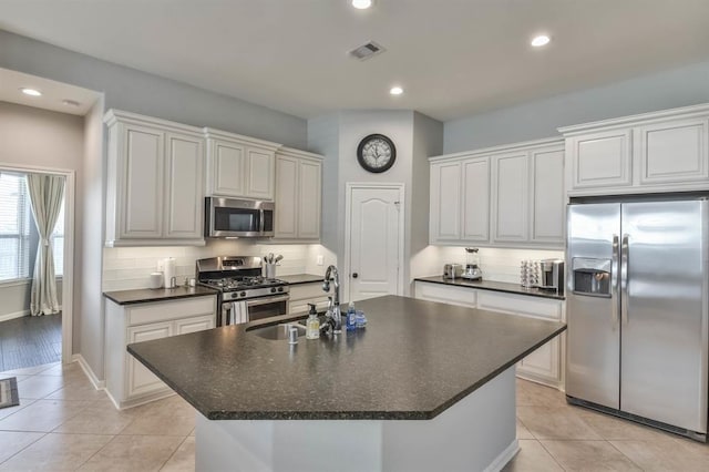 8922 Pinenut Dr, Cypress, TX 77433 - kitchen featuring appliances with stainless steel finishes, dark countertops, a center island with sink, light tile patterned flooring, and recessed lighting