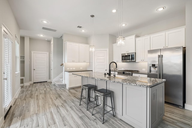 16726 Echo Heights Dr, Cypress, TX 77433 - kitchen featuring stainless steel appliances, light stone countertops, light wood finished floors, white cabinetry, and a center island with sink