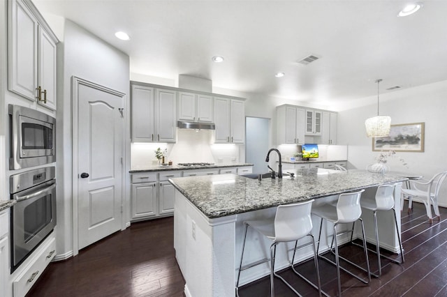 23706 Tristan Bay Ct, Spring, TX 77386 - kitchen featuring appliances with stainless steel finishes, dark wood-style flooring, an island with sink, light stone counters, and hanging light fixtures