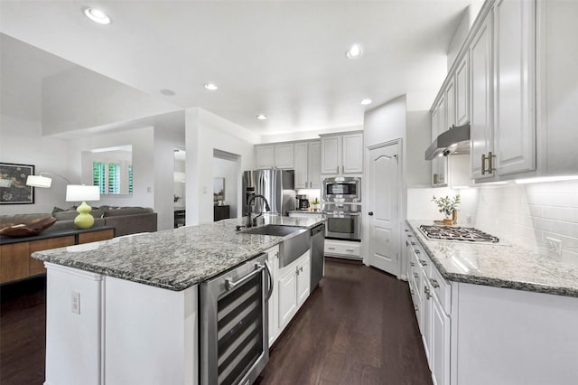 23706 Tristan Bay Ct, Spring, TX 77386 - kitchen featuring wine cooler, appliances with stainless steel finishes, under cabinet range hood, dark wood-style floors, and light stone countertops