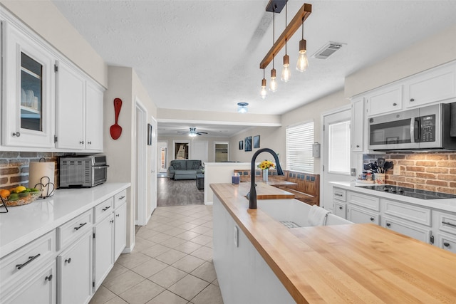 3302 Candlelon Dr, Spring, TX 77388 - kitchen featuring stainless steel microwave, wood counters, black electric stovetop, backsplash, and light tile patterned floors