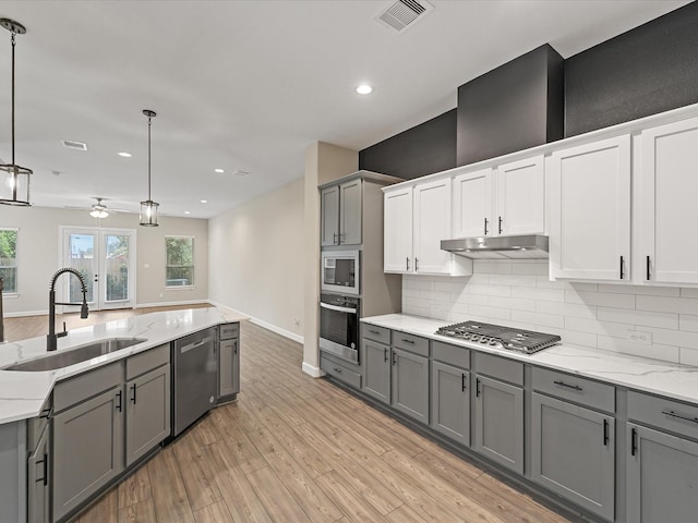 1109 Robbie St, Houston, TX 77009 - kitchen featuring stainless steel appliances, gray cabinets, light wood finished floors, under cabinet range hood, and tasteful backsplash