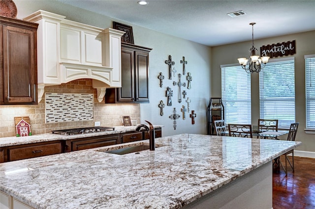 3403 Westhaven Ct, Fulshear, TX 77441 - kitchen featuring a chandelier, light stone countertops, tasteful backsplash, stainless steel gas cooktop, and hanging light fixtures