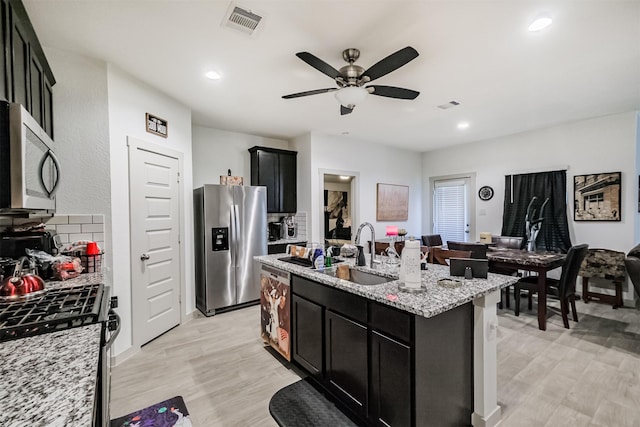 826 Green Clover Ln, Rosharon, TX 77583 - kitchen with stainless steel appliances, dark cabinets, ceiling fan, a kitchen island with sink, and light stone countertops