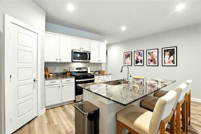 621 Little Spring Ct, Anahuac, TX 77514 - kitchen with appliances with stainless steel finishes, light wood-style floors, a kitchen breakfast bar, dark stone counters, and white cabinetry