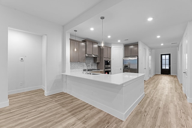 19209 Olive Heath Ln, Magnolia, TX 77355 - kitchen featuring appliances with stainless steel finishes, light wood-style flooring, light countertops, a peninsula, and tasteful backsplash