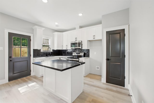 4719 Mallow St, Houston, TX 77033 - kitchen with stainless steel appliances, tasteful backsplash, white cabinets, a kitchen island, and light wood finished floors