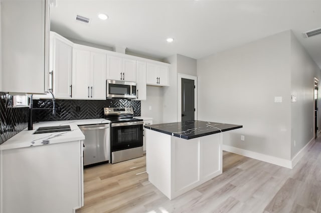 4719 Mallow St, Houston, TX 77033 - kitchen featuring appliances with stainless steel finishes, light wood-style flooring, white cabinetry, decorative backsplash, and a kitchen island